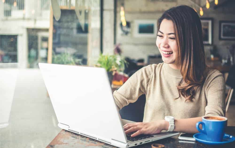 wanita bekerja dengan laptop di dalam cafe sebagai ilustrasi tips memilih software terbaik